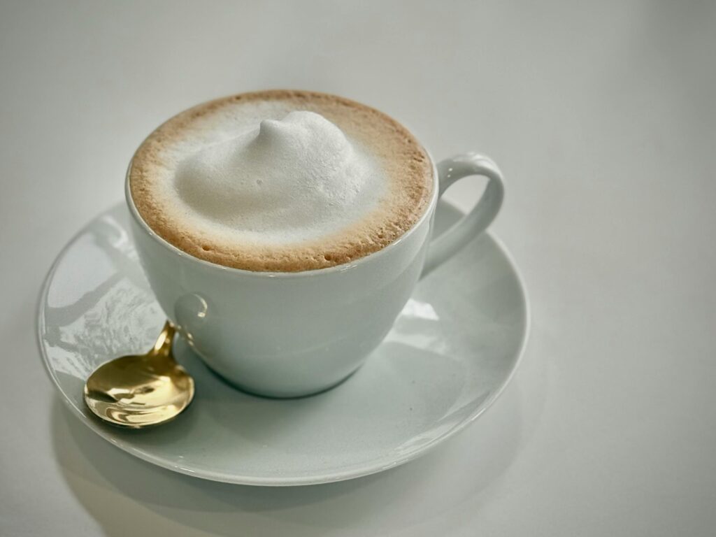 Example Website: Caffa Coffee House Menu Golden spoon and frothy cappuccino in a white cup create a luxurious coffee setting.